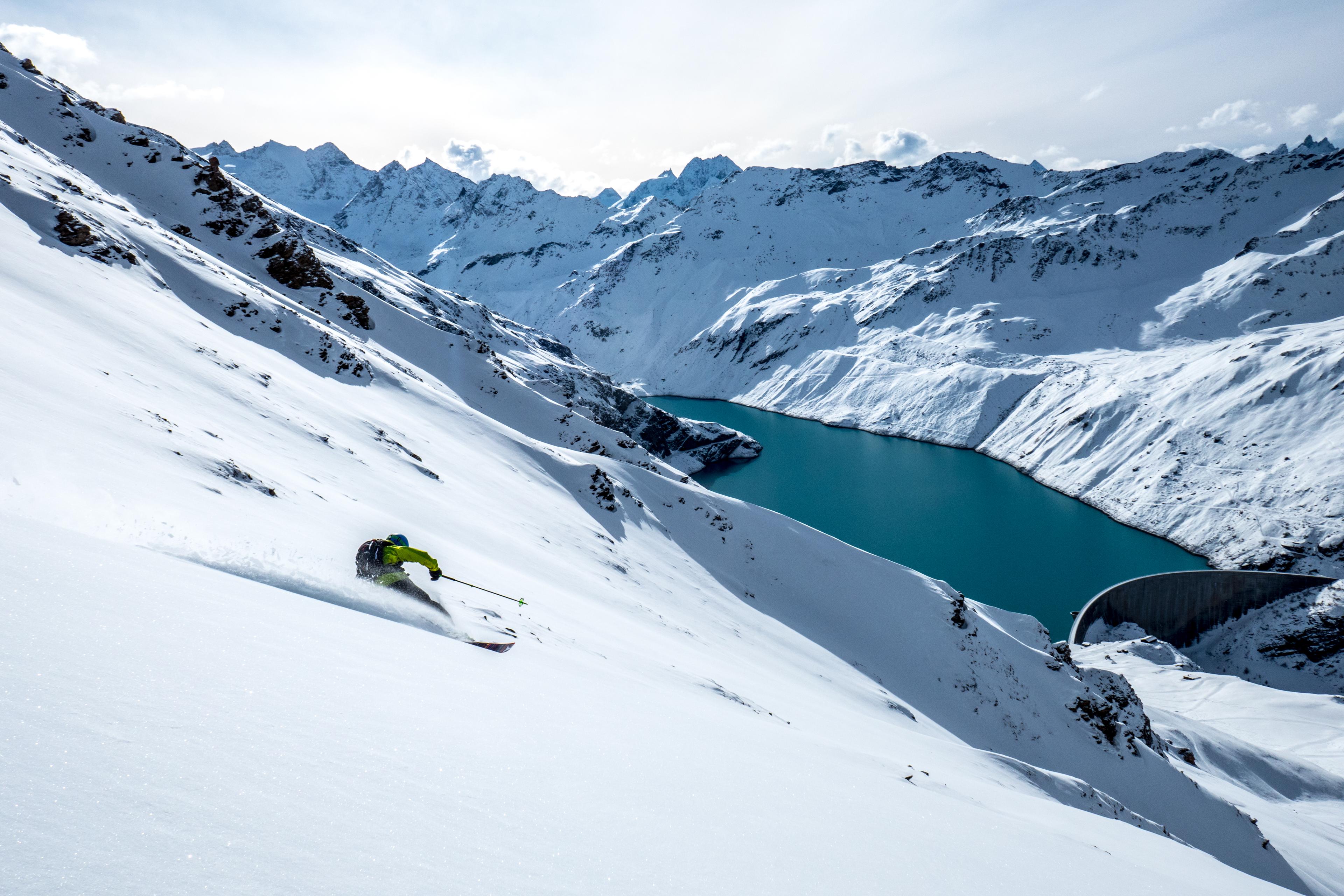 Skiier skiing down off piste slope with lake in background